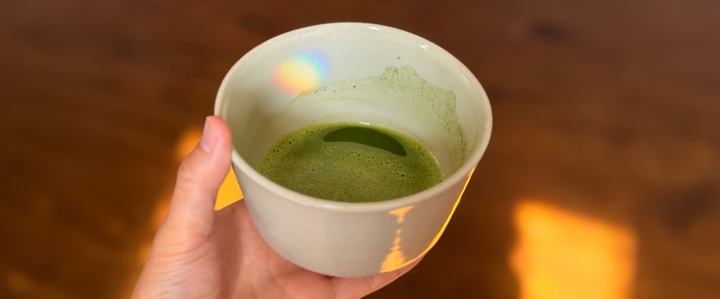 A bowl of matcha held in the hand, on a wooden floor at home