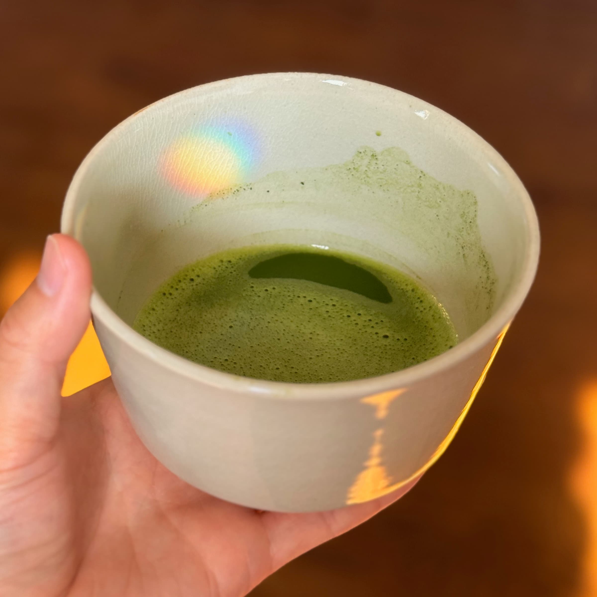 A bowl of matcha held in the hand, on a wooden floor at home