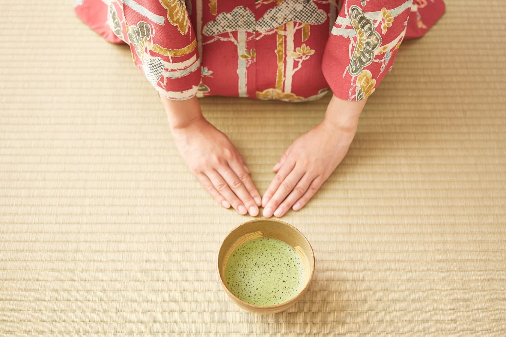 A guest's hands set down on the tatami beside the bowl, in a bow