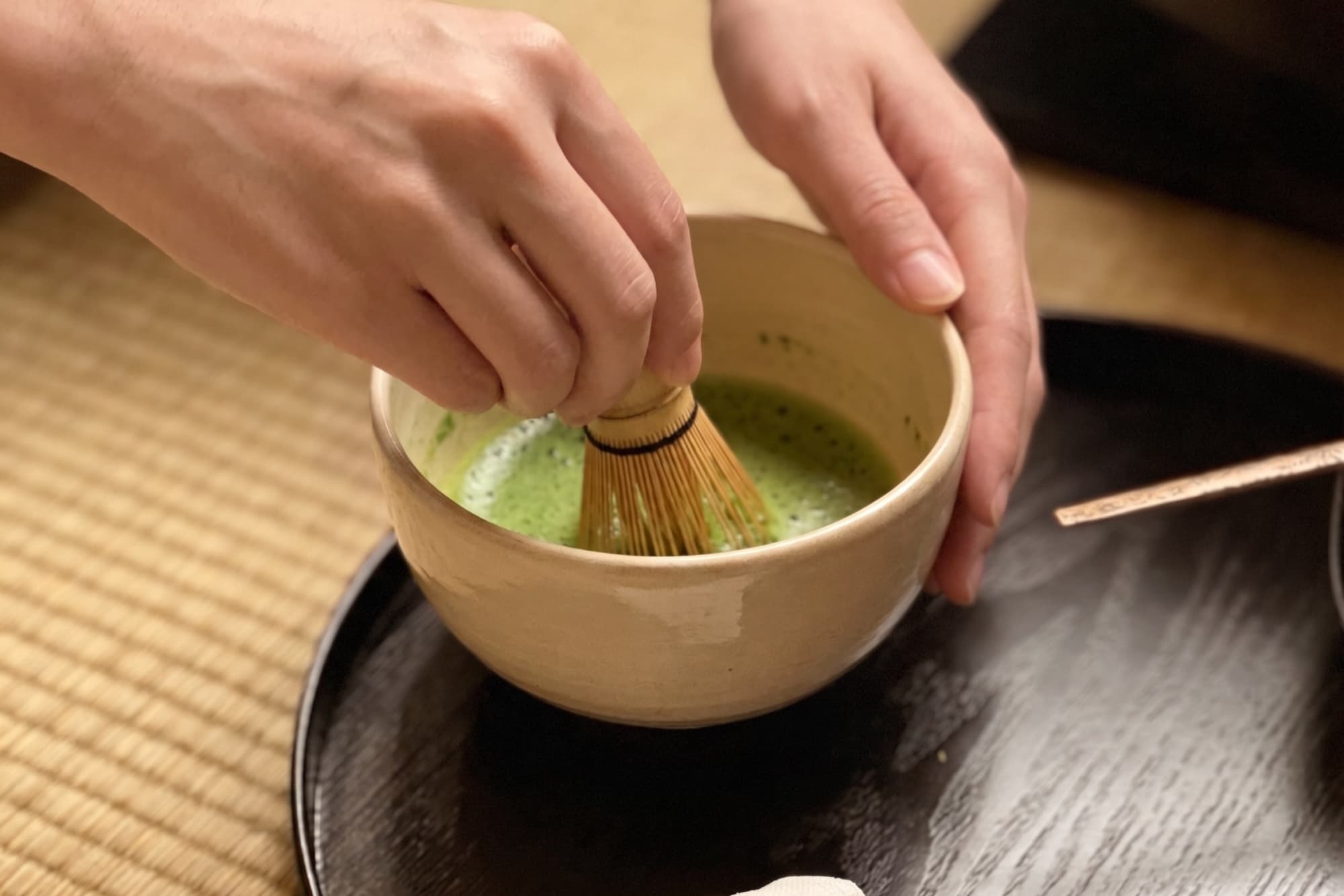 Whisking matcha in the bowl with a chasen, on a lacquer tray